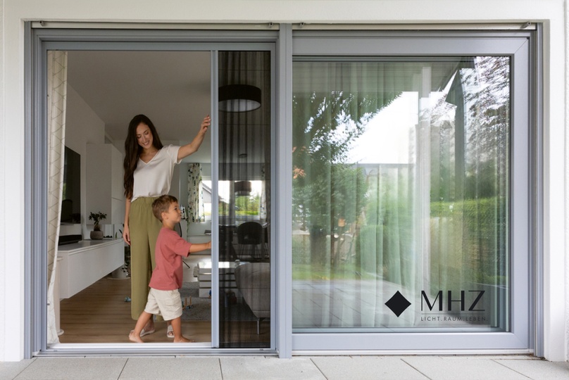 Mutter und Kind öffnen ein Plissetür-Fliegengitter an einer großen Balkontür