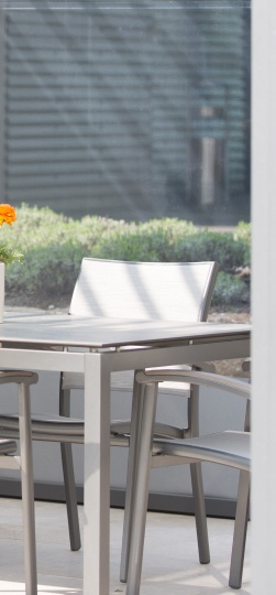 Sonniger Patio mit modernem Tisch, Stühlen, grünen Pflanzen und orangefarbener Blume.
