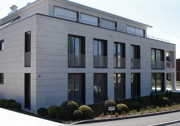 Modernes Steingebäude mit großen Fenstern und gepflegten Büschen.