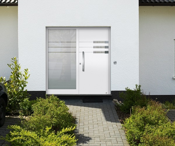 Fotografie: Moderne weiße Haustür mit Glasseitenteil, gepflastertem Weg und grünen Büschen.