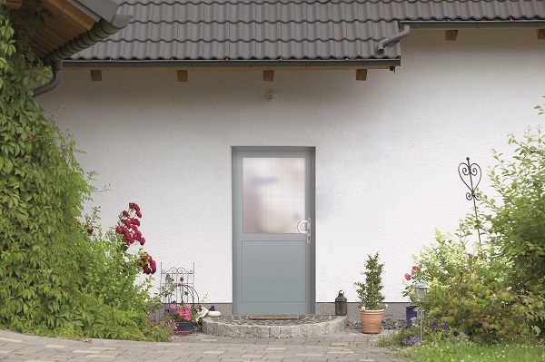 Graue Haustür mit Milchglas in weißer Hauswand, flankiert von üppigem Grün.