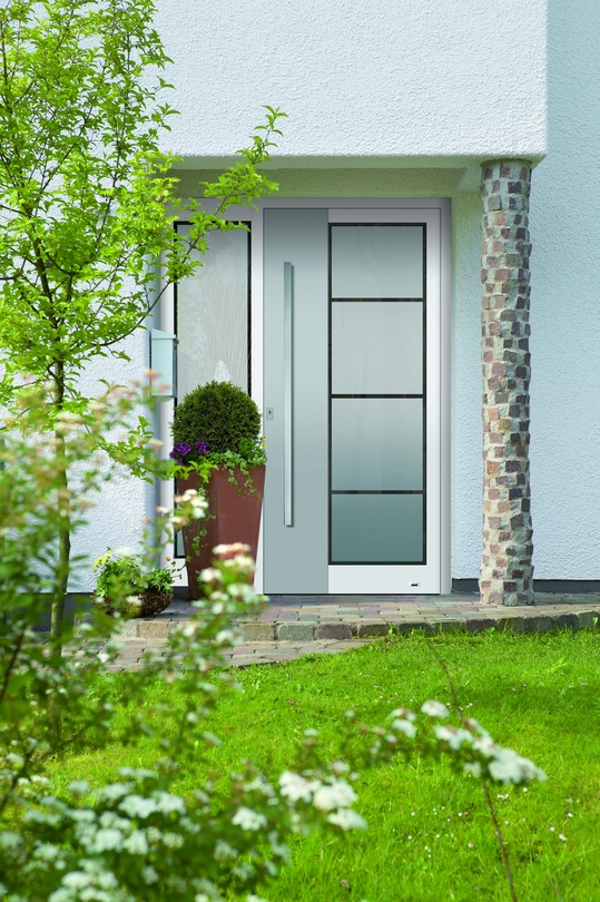 Moderne Haustür mit matter Verglasung, umgeben von grünem Garten.