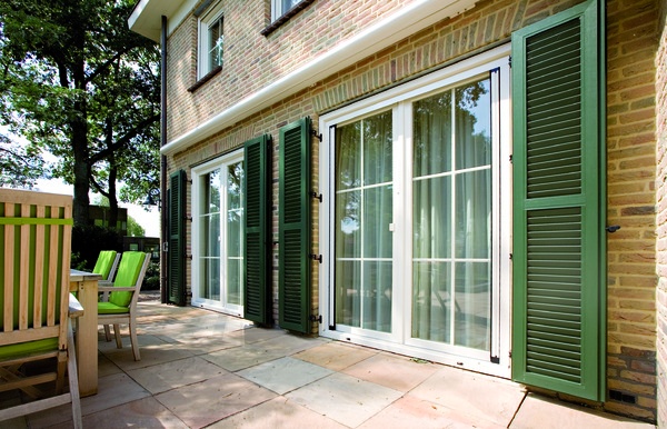 Sonniger Patio vor einem Backsteinhaus mit weißen Fenstern und grünen Fensterläden.