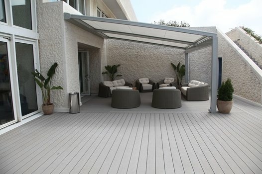 Moderne Terrasse mit hellgrauem Deck, bequemen Lounge-Möbeln unter Pergola und Pflanzen.
