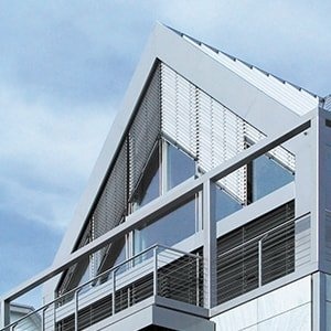 Modernes Gebäude mit dreieckigem Giebel, Jalousien und Balkon vor blauem Himmel.