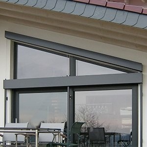 Moderne Gebäudefront mit dreieckigen Fenstern, grauem Sonnenschutz und Balkon.
