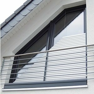 Schräges Fenster an weißer Fassade mit diagonalen Lamellen und Balkongeländer.