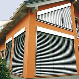 Orangefarbenes Haus mit modernen, silbernen Außenjalousien.