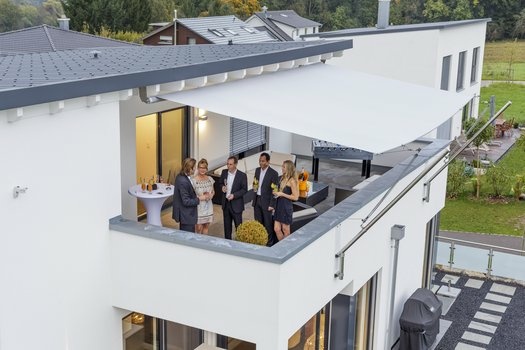 Fünf Personen feiern auf modernem Balkon unter weißer Markise.