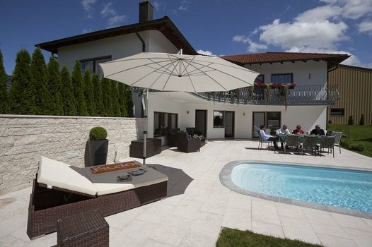 Sonnige Villa mit Pool, Terrasse, Liege und Essgruppe, umgeben von Grün.