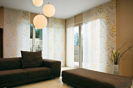 Geräumiges Wohnzimmer mit dunklem Sofa, goldgemusterten Schiebevorhängen und Pendelleuchten.