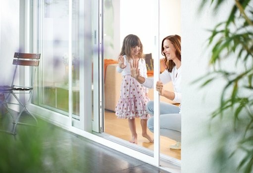 Glückliche Mutter und lächelndes Kind an offener Glastür zum Garten.