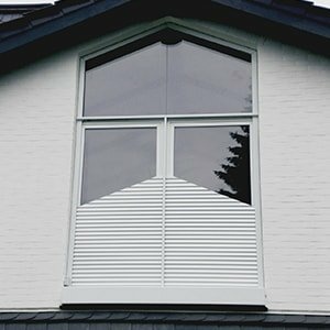 Weißes Haus mit großem Fenster. Unten weiße Lamellenjalousien, die eine V-Form bilden.