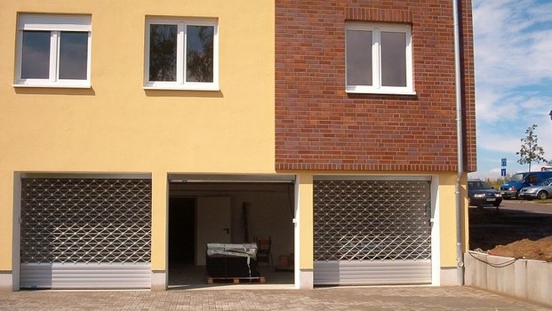 Neues Gebäude, gelb und rot, mit drei Rollgittertoren; das mittlere ist geöffnet.