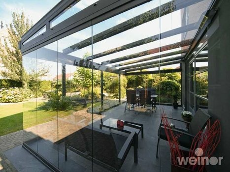 Heller Glas-Wintergarten mit moderner Einrichtung, umgeben von einem grünen Garten.