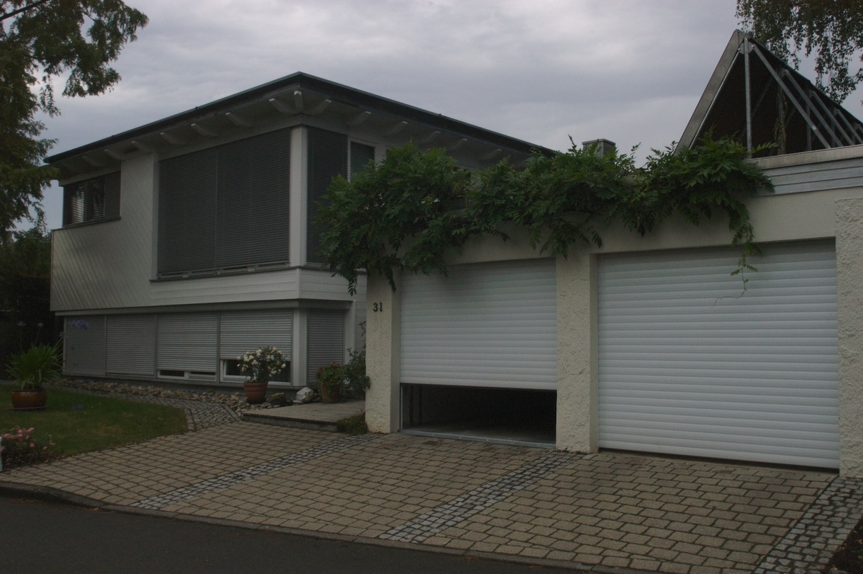 Modernes Haus mit Doppelgarage, ein Garagentor ist teilweise geöffnet.