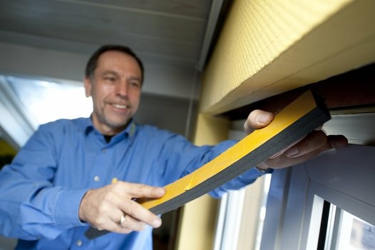 Lächelnder Handwerker dichtet Fensterrahmen mit gelbem Werkzeug ab.