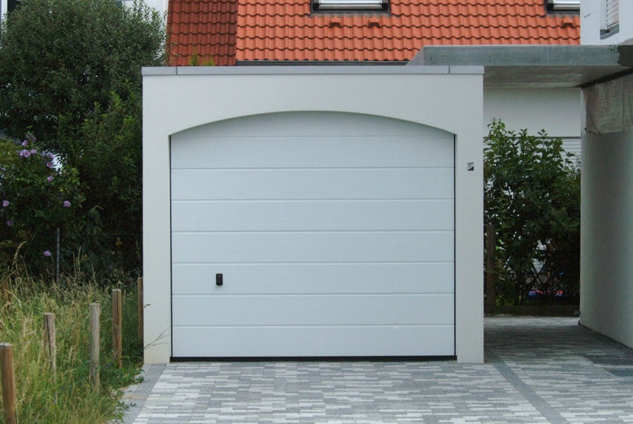 Moderne weiße Garagentür mit Bogen und gepflasterter Auffahrt.