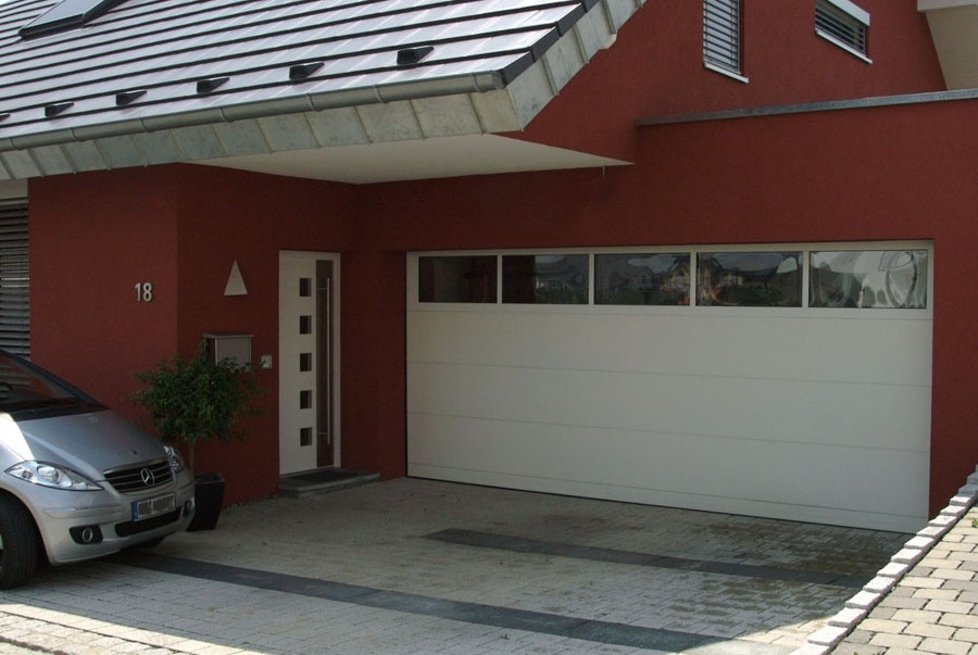 Modernes rotes Haus mit weißem Garagentor und silbernem Auto auf der Einfahrt.