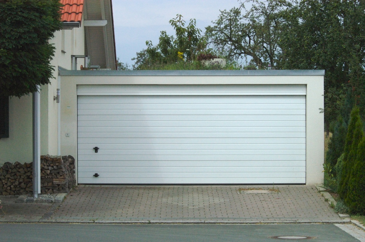 Weißes Garagentor mit gepflasterter Zufahrt und begrüntem Flachdach.