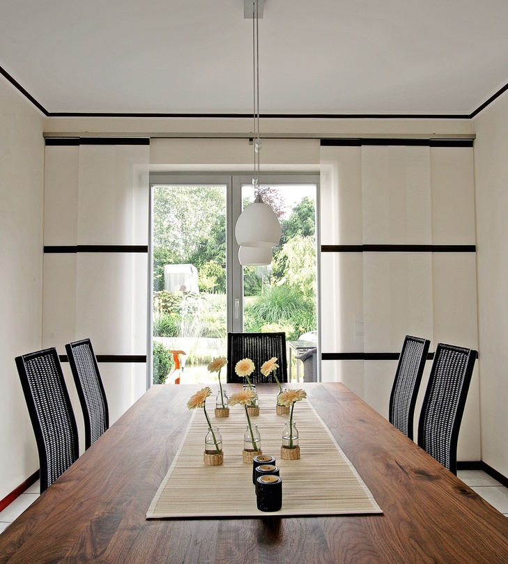 Helles Esszimmer mit Holztisch, Blumendeko und Glastür zum Garten.