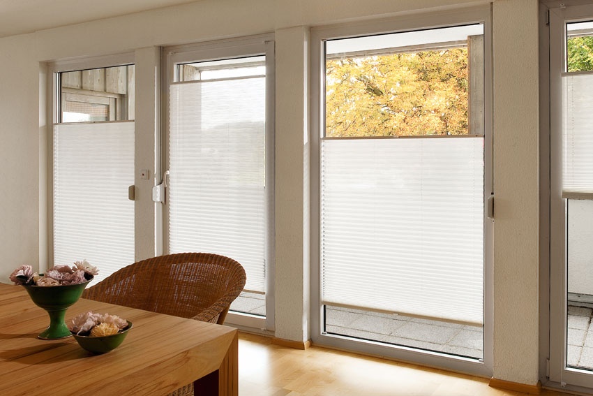 Heller Raum mit Glastüren und weißen Plissees; dahinter gelbe Herbstblätter.