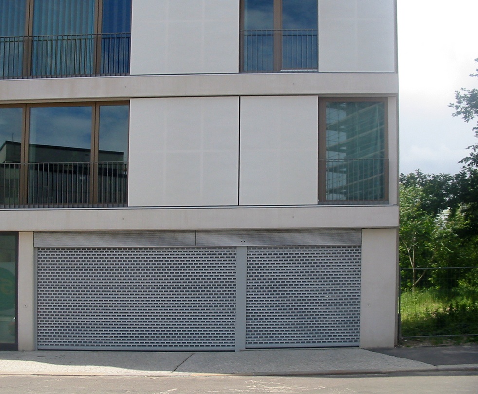 Moderne Gebäudefassade mit zwei grauen Rolltoren und Fenstern.