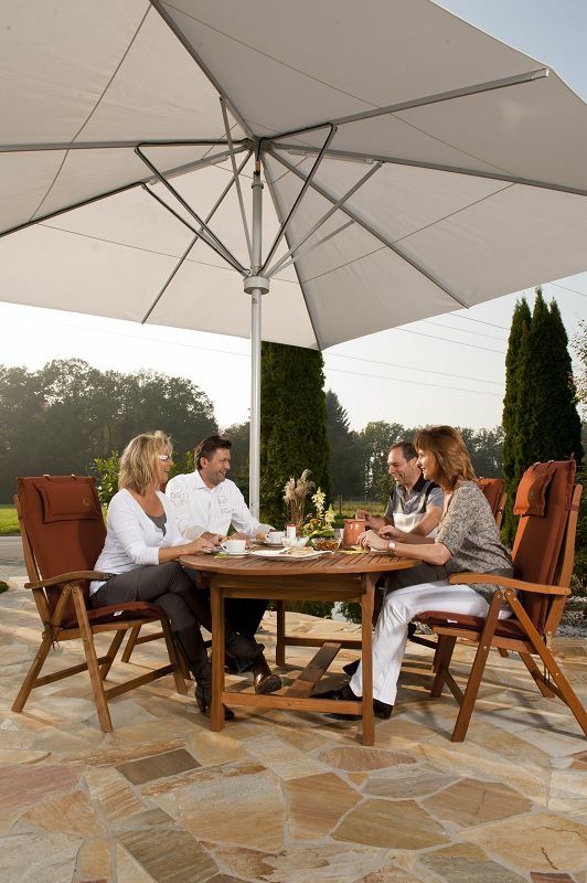 Vier Personen sitzen entspannt an einem Holztisch unter einem großen weißen Sonnenschirm.