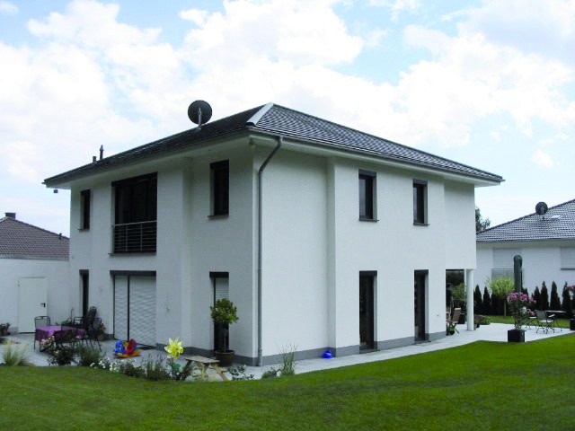 Modernes, weißes zweistöckiges Haus mit dunklem Dach und grünem Rasen.