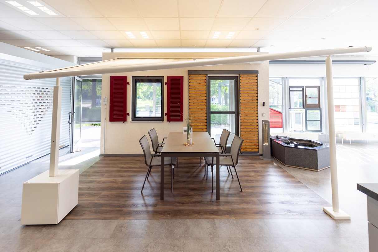 Heller, moderner Showroom mit Fenstern, roten Rollläden, Esstisch und großer Lichtkonstruktion.
