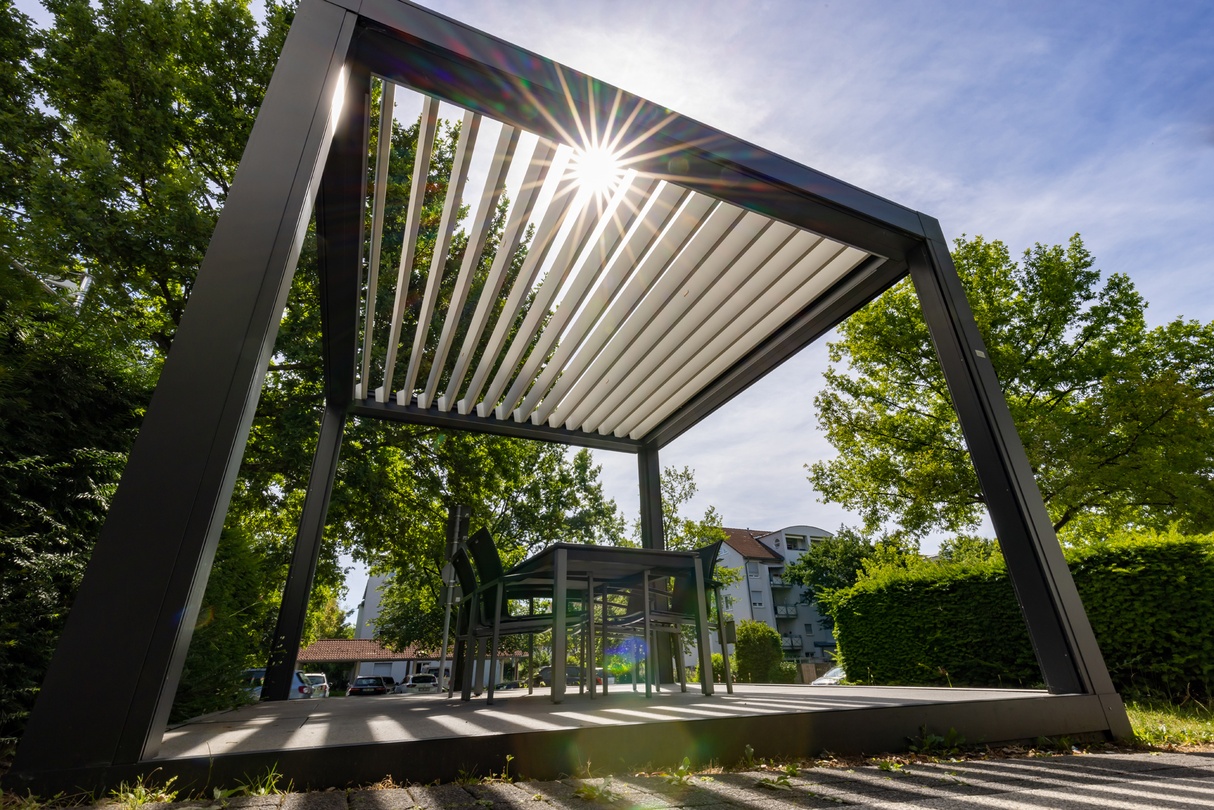 Moderne graue Pergola mit Lamellendach, Sonnenstern und Sitzgruppe im Freien.