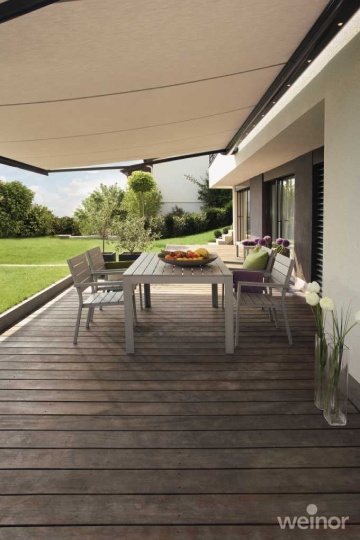 Geräumige Holzterrasse mit großer, ausfahrbarer Markise und Essbereich vor grünem Garten.