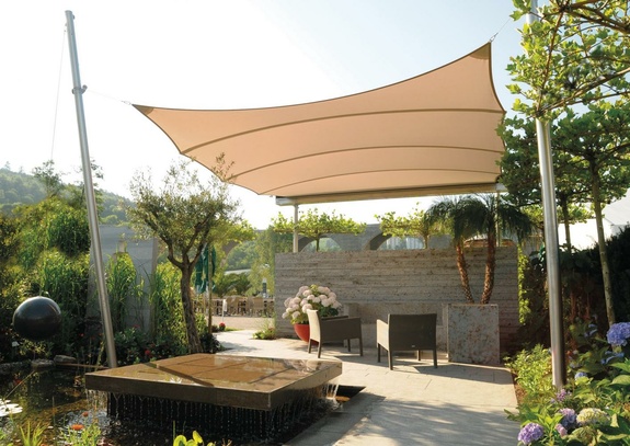 Einladende Gartenoase mit beigem Sonnensegel, Wasserspiel und bequemen Lounge-Möbeln.