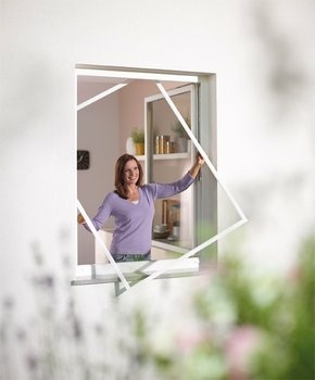 Frau installiert lächelnd ein weißes Insektenschutzgitter am Fenster.