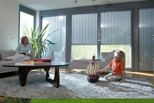 Frau und Junge spielen entspannt in hellem Wohnzimmer mit Vertikaljalousien.