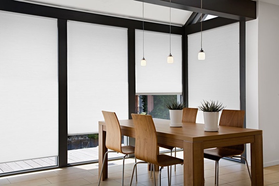 Modernes Esszimmer mit Holztisch, großen Fenstern und weißen Rollos.