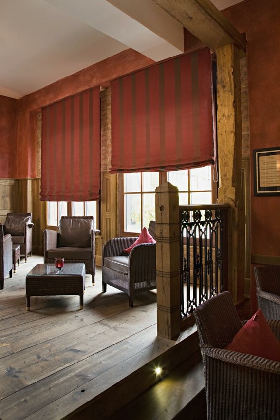 Rustikale Lounge mit dunklen Ledersesseln, Holzboden, roten Wänden und gestreiften Rollos.