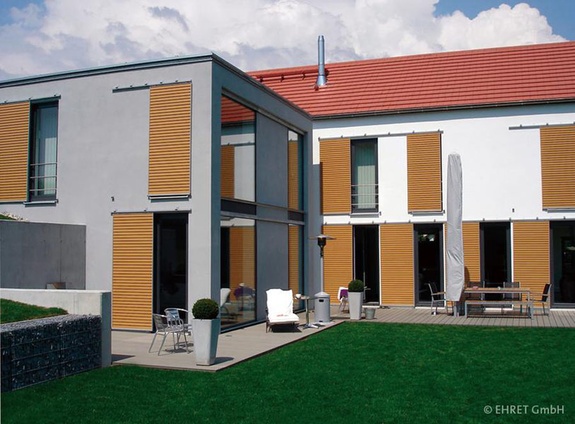 Fotografie eines modernen Hauses mit orangefarbenen Rollläden und grünem Garten.