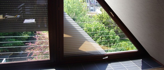 Zwei Dachfenster; das rechte offen mit Blick auf grüne Bäume, das linke mit Jalousien.