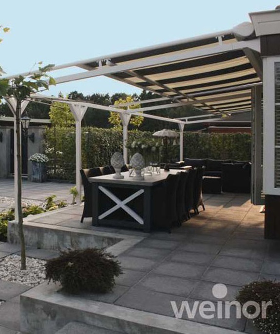 Gepflegte Terrasse mit Esstisch, dunklen Stühlen und Pergola-Sonnenschutz.