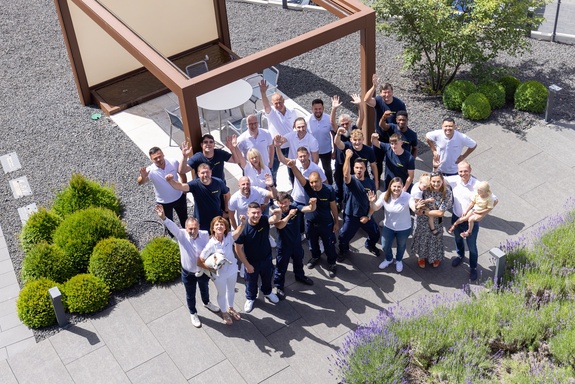 Mettler-Team winkt freundlich neben einem modernen braunen Pavillon