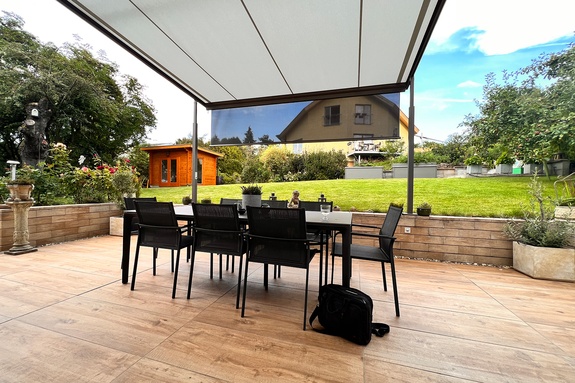 Eine textile Pergola-Markise beschattet den Essbereich und schützt auch bei tiefstehender Sonne