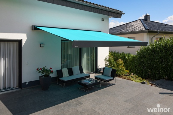 Aufgefahrene Markise spendet Schatten über Sitzmöbeln auf der Terrasse