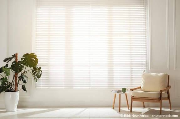 Großes Fenster mit innenliegenden Lamellenjalousien, durch die Sonnenlicht scheint