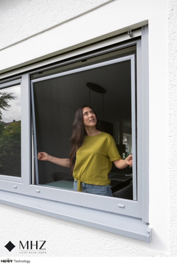 Frau setzt ein Spannrahmen-Fliegengitter im Fenster ein