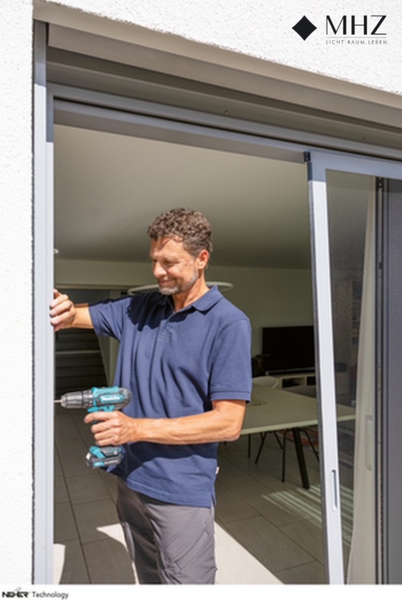 Fachmann bohrt am Fensterrahmen, um Fliegenschutz anzubringen
