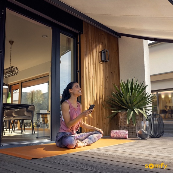 Frau beim Yoga auf der Terrasse fährt die Markise per Smartphone aus