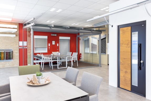 Moderner Showroom mit Terrassenmöbeln, Überdachung und dunkler Haustür.