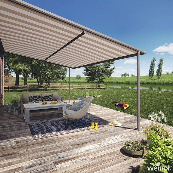 Pergola-Markise beschattet den Sitzbereich einer Terrasse mit offenen Wiesen dahinter