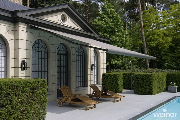 Moderne Gelenkarmmarkise beschattet die Liegen vor einem Pool am Haus